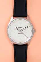 Studio image of a Bower tide watch with a coral white textured dial, white hour markers, tide markings, and a black leather strap, displayed on a white background.