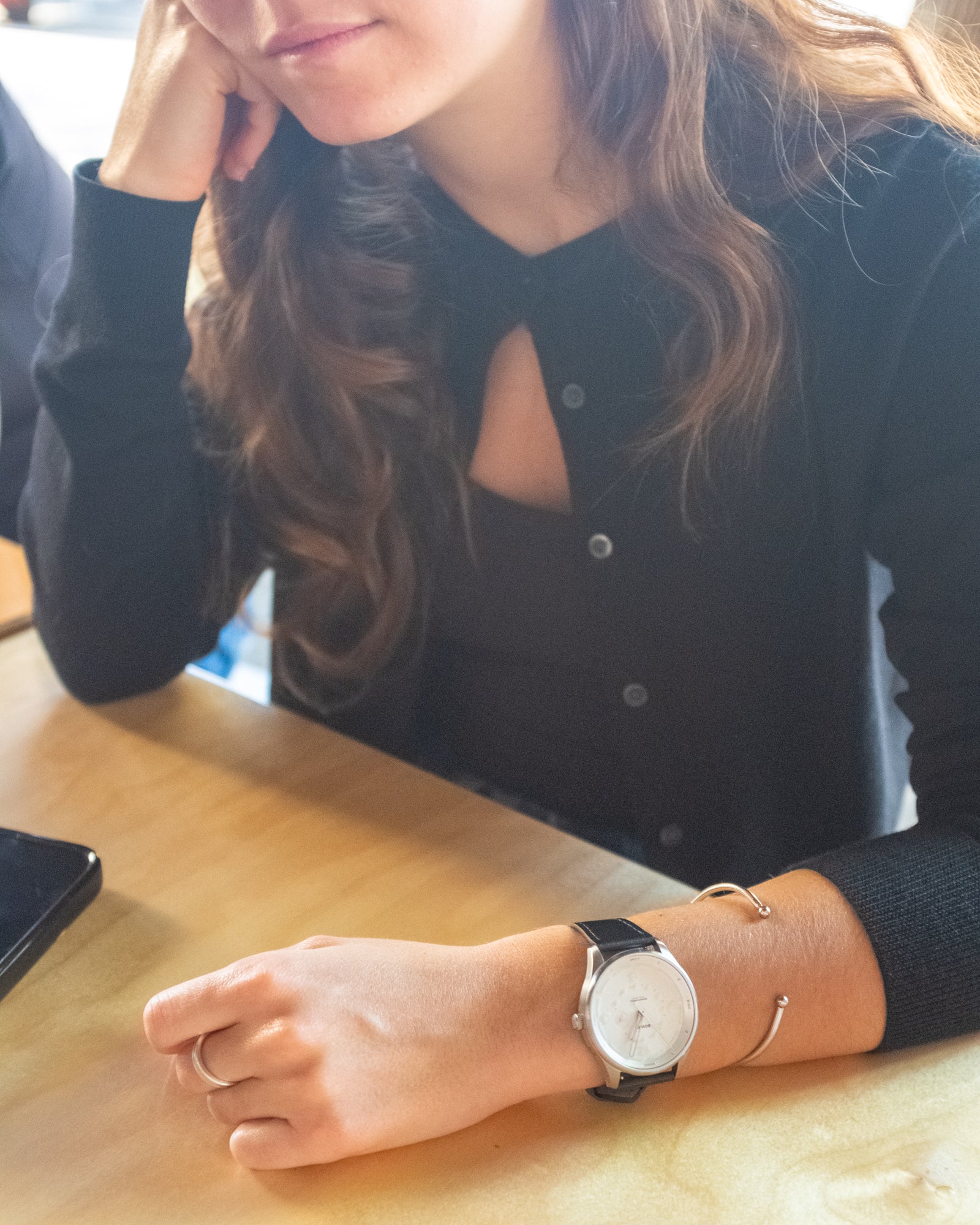 young woman smiling wearing a white watch at a cafe