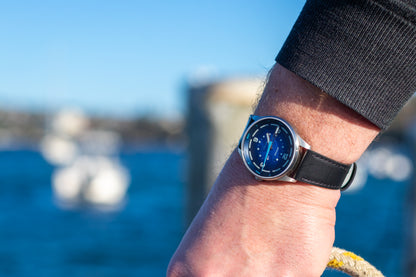 a man in his 40s wearing a blue dial bower watch holding a yellow rope on a dock