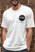 Smiling person wearing a white Bower Watches T-shirt with a black circular logo on the chest that reads “BOWER WATCHES” and “TIDE SEEKER / 2024,” standing in front of a brick wall.