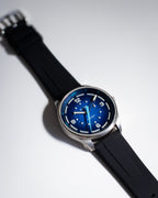 Deep Blue Tide Seeker watch by Bower with black rubber strap, displayed on a clean white background with dramatic shadow. Showcases the watch’s semidiurnal tide-tracking dial and robust, ocean-ready design.