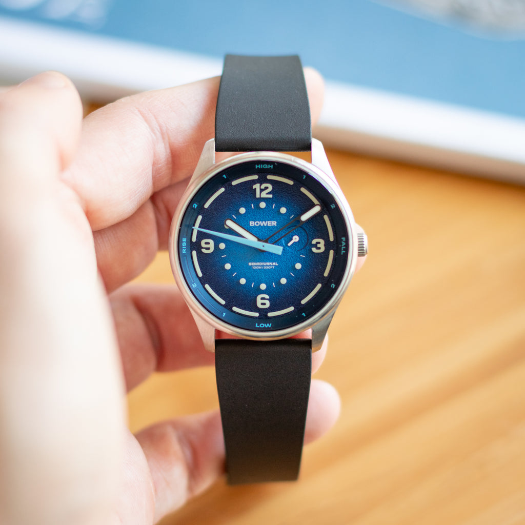 Hand holding a bower tide seeker watch with a blue face and CTS FKM Rubber strap on a blurred background