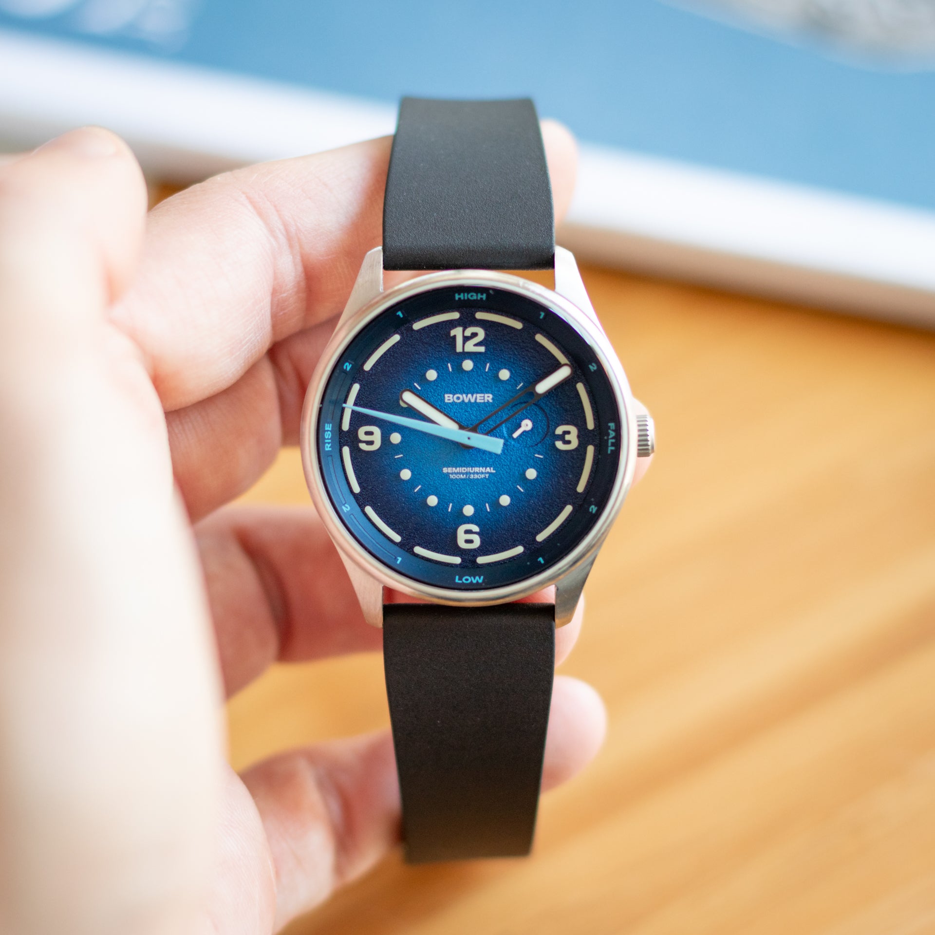 Hand holding a bower tide seeker watch with a blue face and CTS FKM Rubber strap on a blurred background