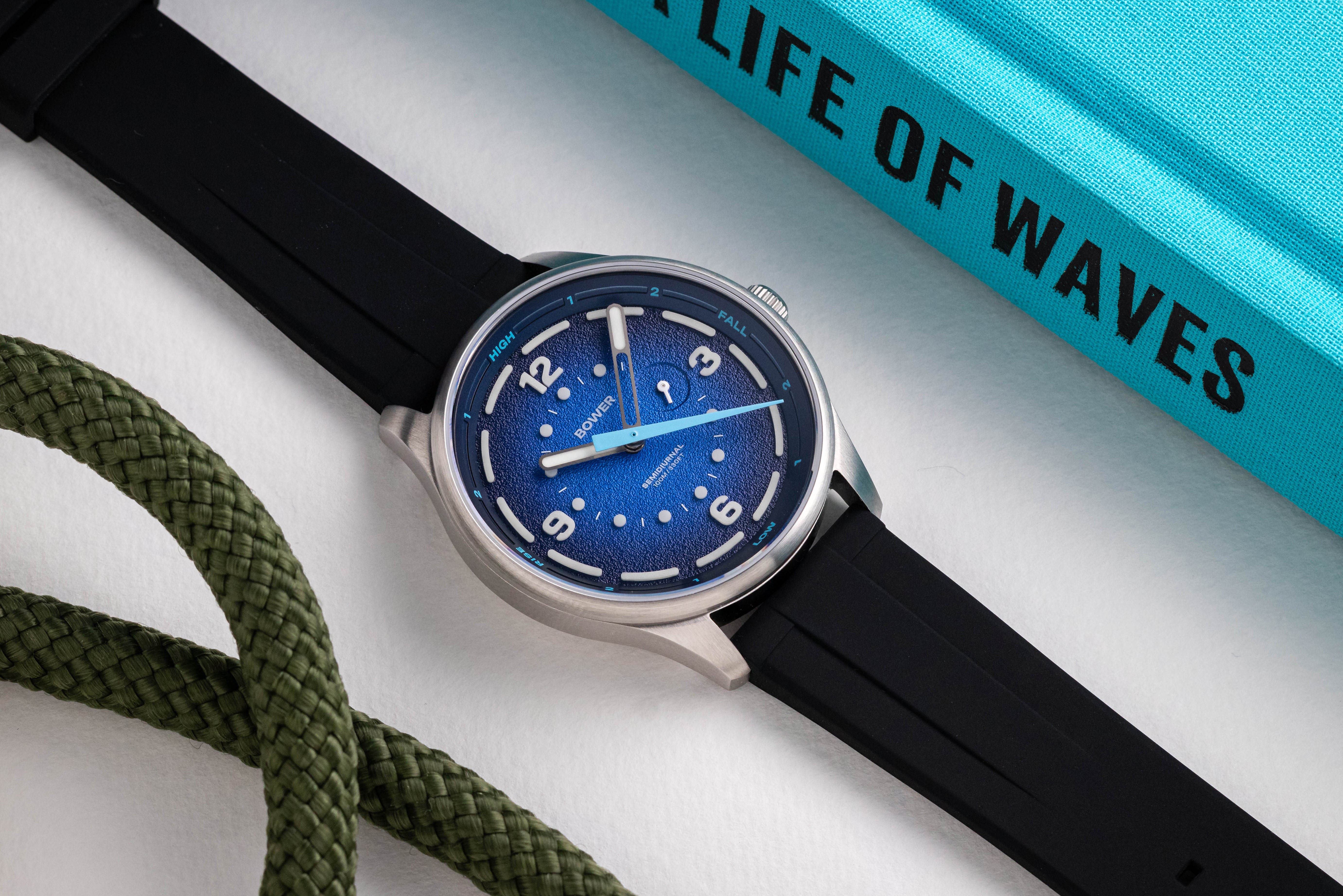 Close-up of the Bower Tide Seeker watch with a deep blue textured dial, semidiurnal tide hand, and white luminous markers, paired with a black rubber strap.