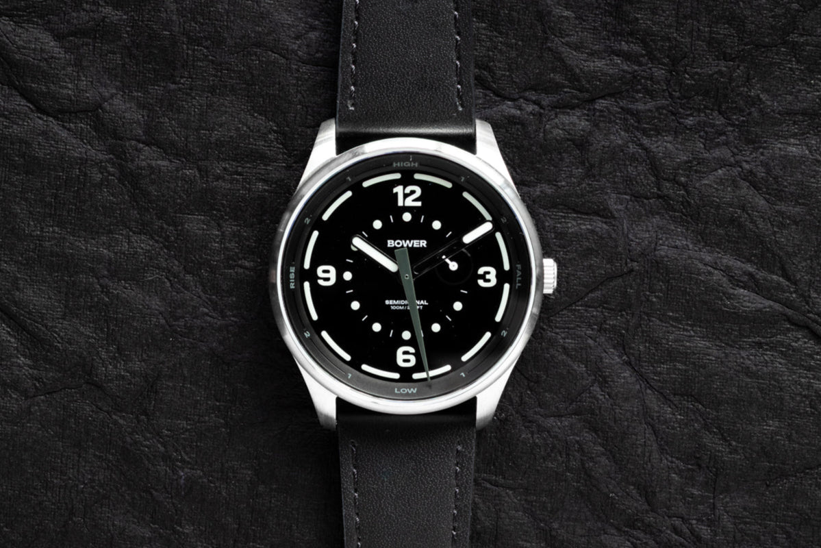 Midnight Black Tide Seeker watch by Bower with black leather strap, centered on a dark textured background. Premium semidiurnal tide-tracking watch designed for ocean adventurers.