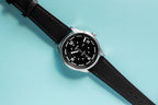 Midnight Black Tide Seeker watch by Bower with black leather strap, displayed on a light blue background. Minimalist tool watch designed for tide tracking and coastal adventures.