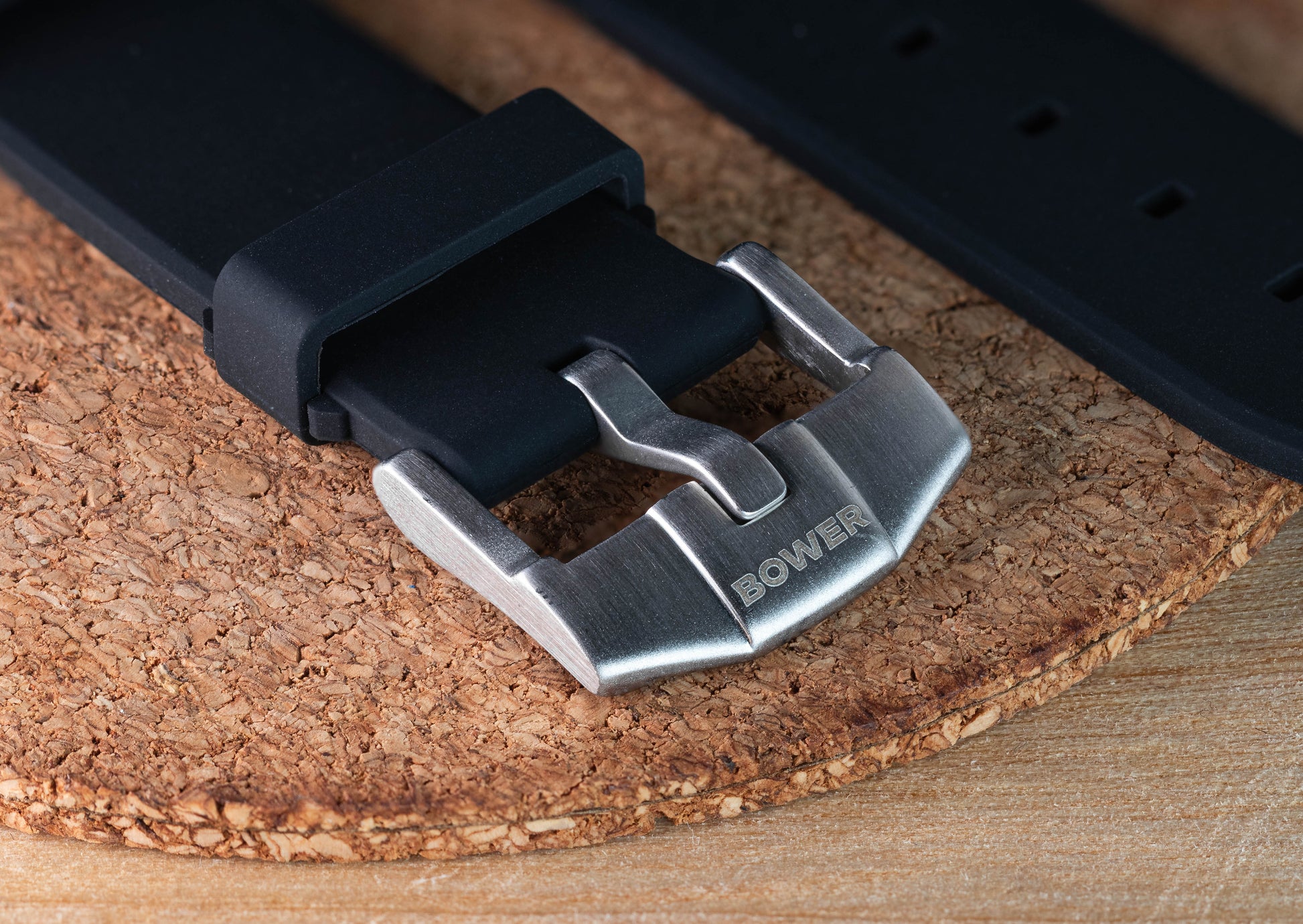 Close-up of Bower-branded stainless steel buckle on black rubber watch strap, resting on cork mat. Durable strap option for Tide Seeker ocean watches.